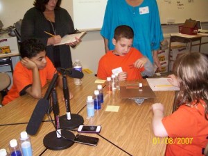 Students investigating how the liquids move and change in bottles as they roll down a clipboard ramp. A data collector and teacher Sue Osborne (blue shirt) watches the students' reactions.
