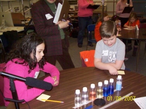 Students observing the properites of a liquid in bottles before investigating them as a data collector looks on.